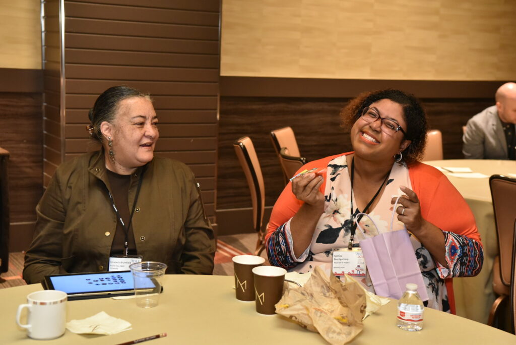 Two women seated at a table, smiling, during a break at 2018 Forum