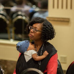 DLF Advisory Committee member Stacie Williams listens to keynote while holding infant chiild